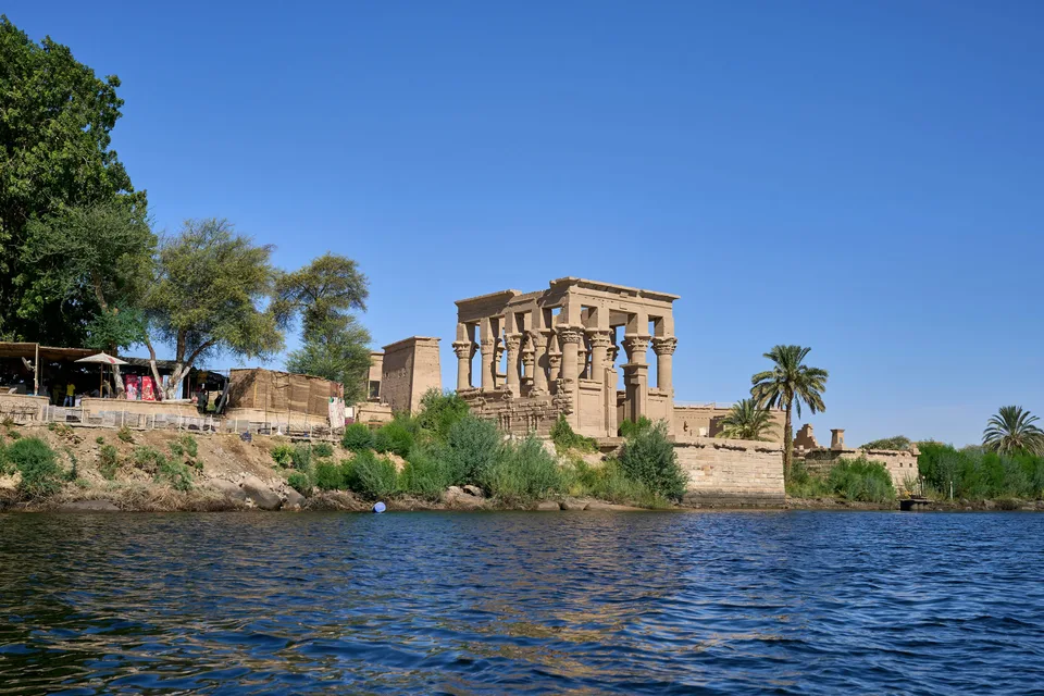 Ancient temple columns and palm trees beside the blue Nile