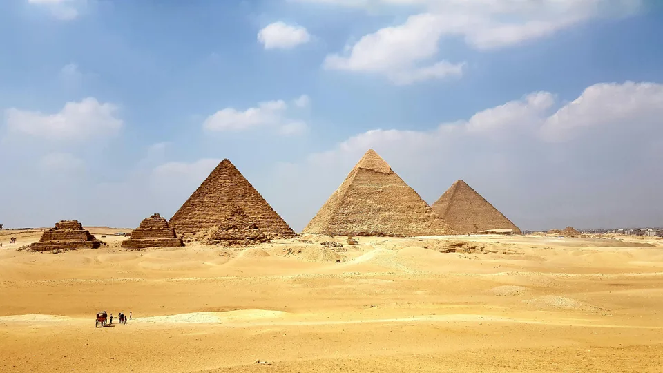 The pyramids of Giza across the sunlit desert beneath a blue sky