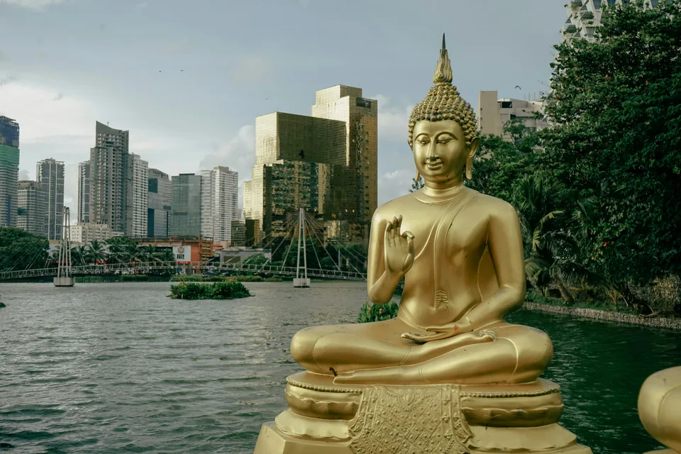 A golden Buddha statue beside a lake and the Colombo skyline