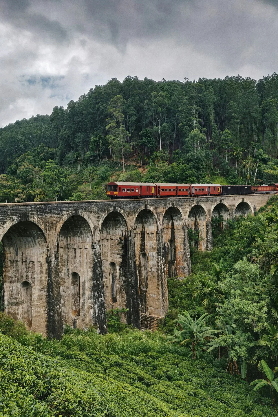 A red train crossing the stone arches of the Nine Arch Bridge