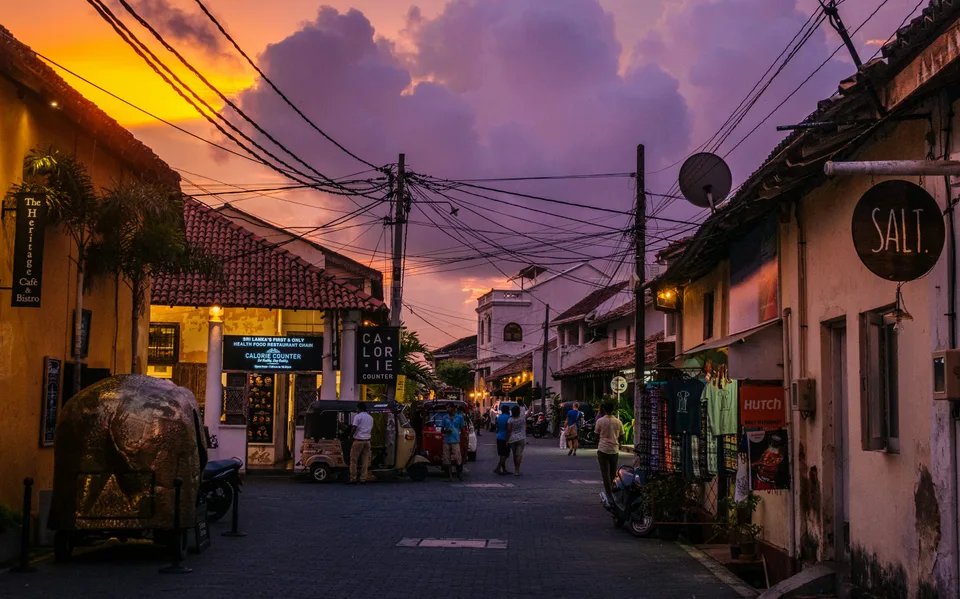A lively street in Galle under a pink and purple evening sky