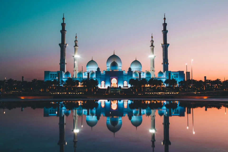 Illuminated mosque domes and minarets reflected in water at dusk