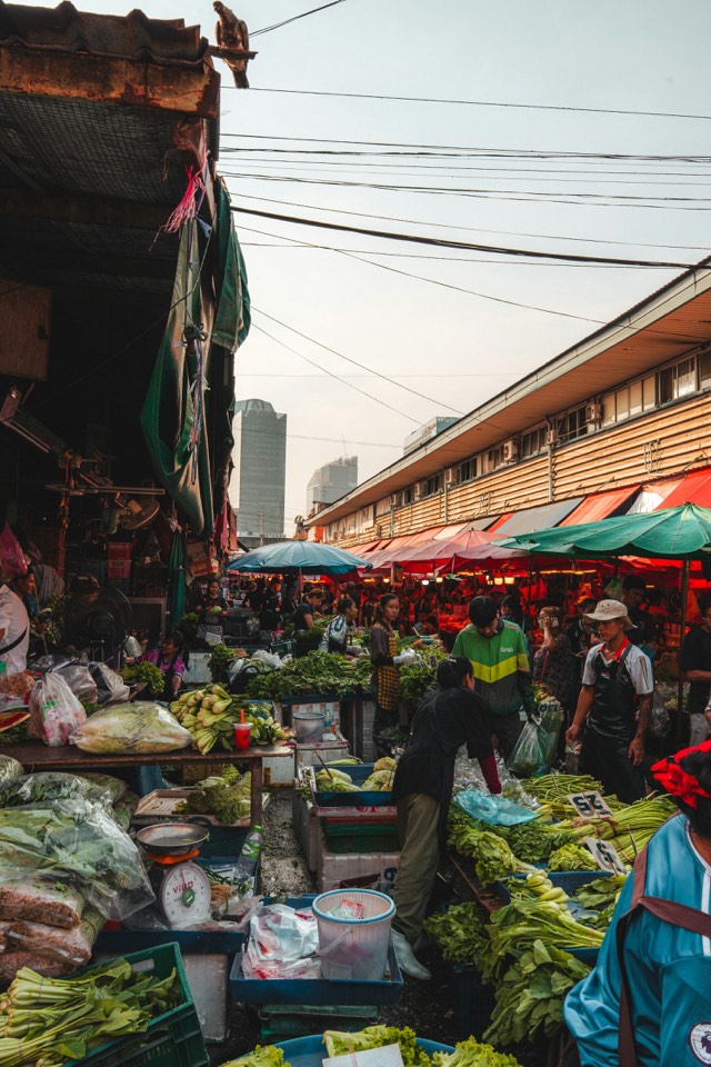 Stalls of fresh produce under awnings at a Bangkok street market