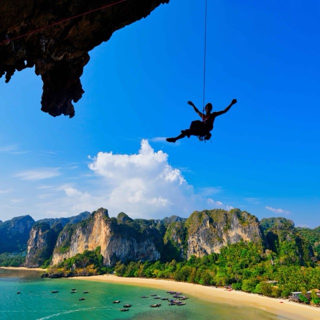 A climber on a limestone overhang above Railay beach in Krabi